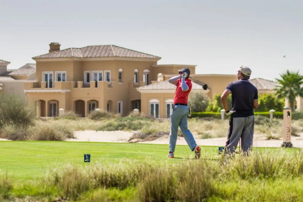 Two men golfing on a green with luxury villas in the background at Arabian Ranches, Dubai.