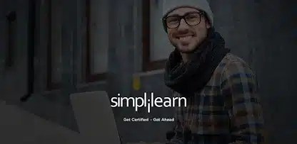 A smiling man with glasses sits at a laptop outdoors, wearing a winter scarf and hat, promoting the Simplilearn online learning platform.